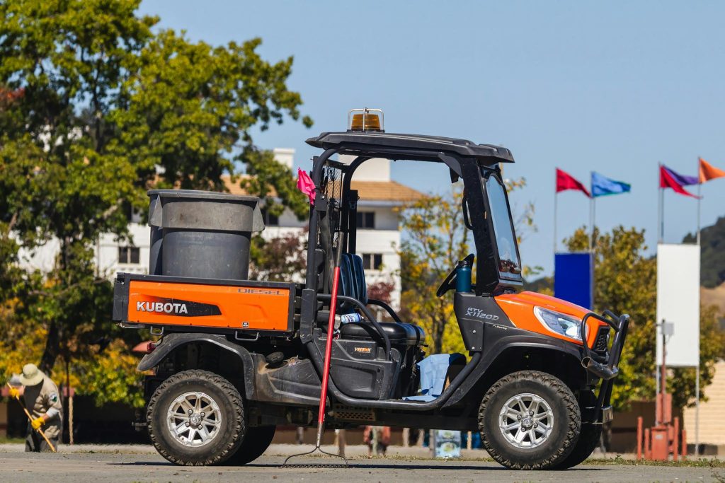 Orange Kubota RTV on display outdoors with flags in the background.